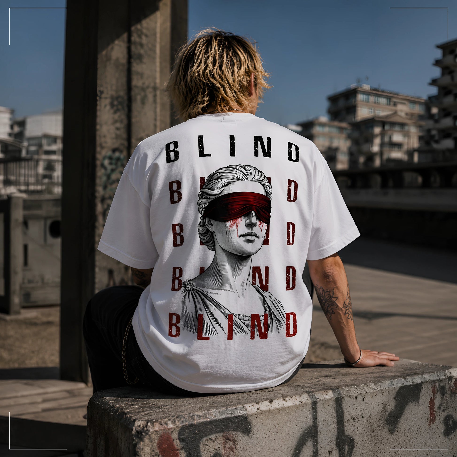 Rodney Logan BLIND weißes Oversized Streetwear-T-Shirt mit großer Blindfold-Grafik und rotem Schriftprint auf der Rückseite, getragen von einem sitzenden Model.