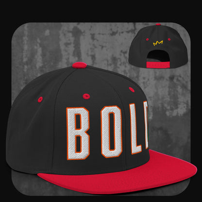 Schwarze Snapback-Cap mit roter Krempe, roten Ösen und rotem Knopf. Auf der Vorderseite „BOLD“ in weißen Blockbuchstaben mit oranger Umrandung, hinten gelbes Kronenlogo.