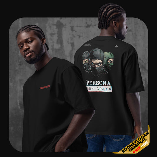 Man wearing a black oversized t-shirt with a red “CLASSIFIED” label on the front and a large illustrated graphic on the back showing three masked figures and the text “PERSONA NON GRATA.”