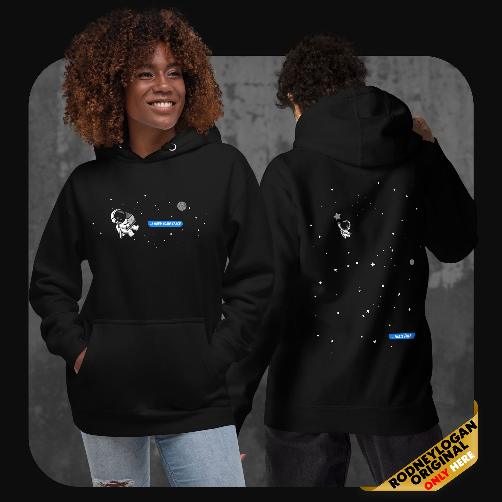 Lifestyle image showing two models wearing the black “I Need Some Space” hoodie – one facing forward with the astronaut and message on the chest, the other turned around revealing the back design with stars and the distant astronaut.