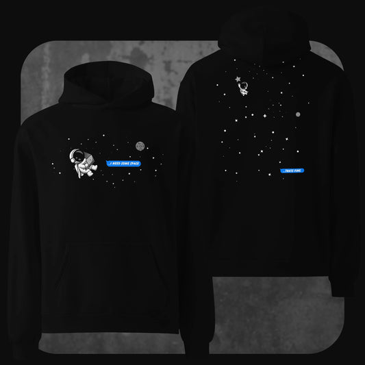 Front and back view of a black oversized hoodie featuring a minimalist outer space theme. The front shows a small cartoon astronaut floating in space with the text bubble “I NEED SOME SPACE” in blue. The back displays the astronaut drifting farther among stars with a reply bubble that says “THAT’S FINE” also in blue.