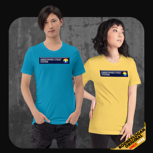 Two models wear colorful t-shirts with a “Christopher Street Station” design and a rainbow subway icon; the man in aqua blue and the woman in yellow stand confidently in front of a textured background.