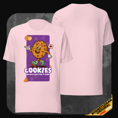 Pastel pink t-shirt displaying a playful chocolate chip cookie with arms, sneakers, and a cheerful face. Below, the phrase “Cookies – Because adulting is hard.”
