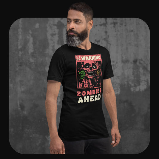 Man wearing a black T-shirt with a vintage-style zombie graphic and the text “WARNING ZOMBIES AHEAD” on the chest, standing against a textured concrete wall.